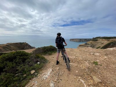 A man standing with his bike overlooking the cliffs at Sagres